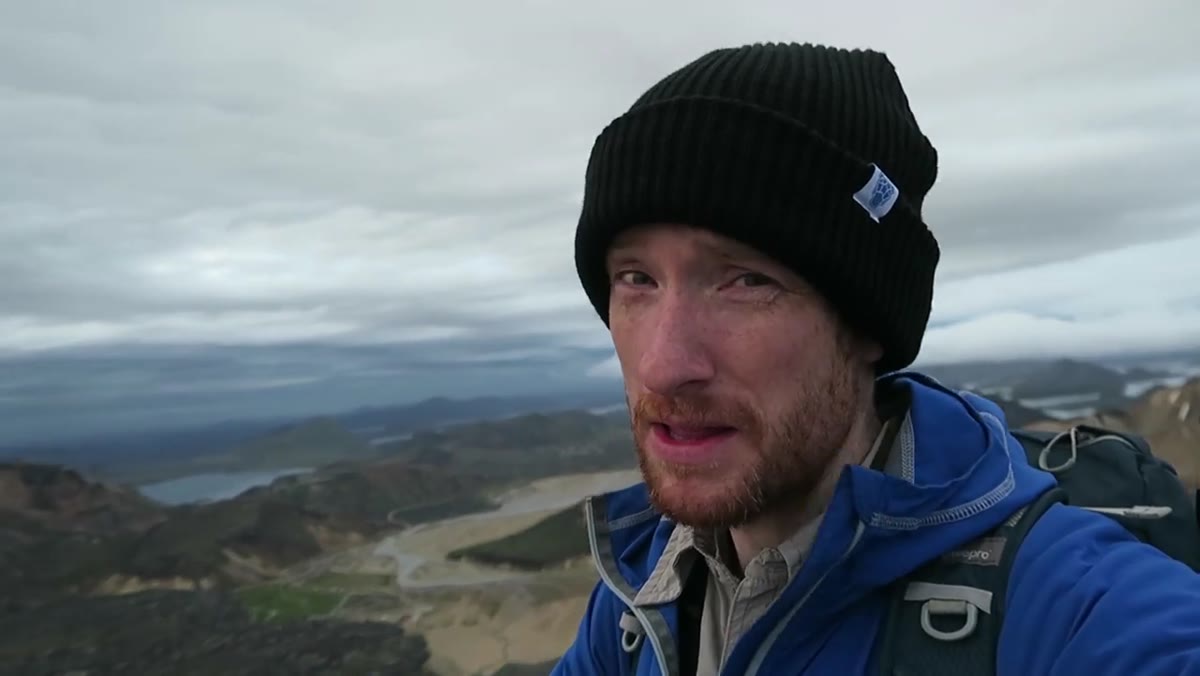 Heaton setting up at the summit, storm sky filling the frame above the landscape